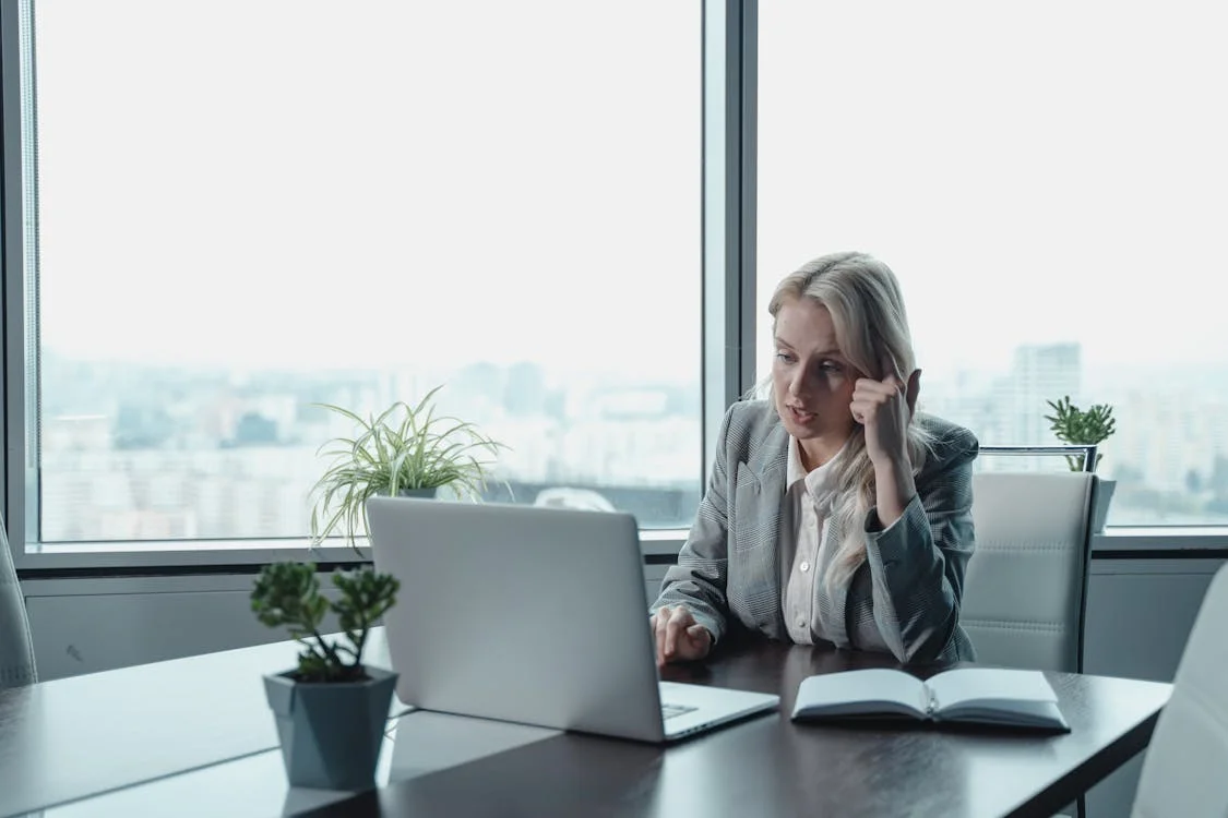 A professional woman working on her laptop at a clean office desk, building her startup profile
